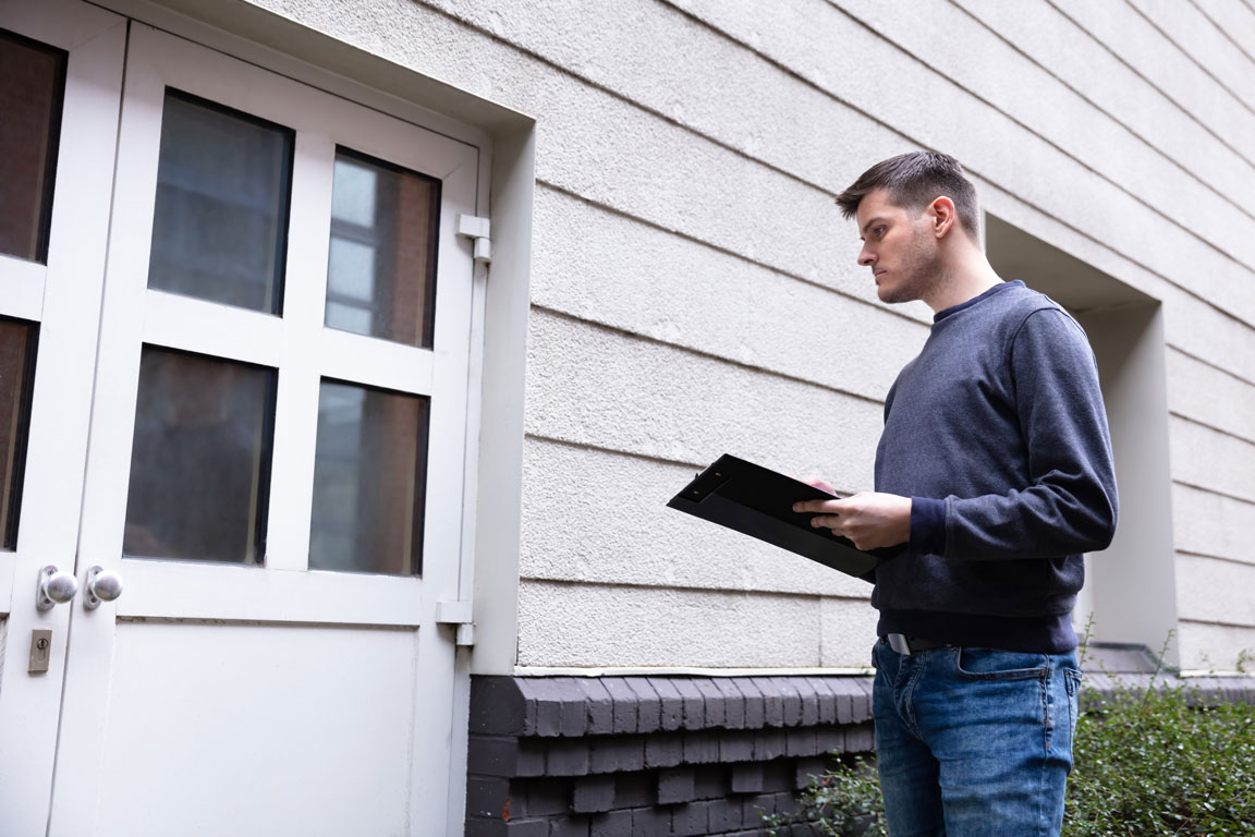 man inspecting the outside of a home for air leaks