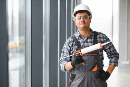 Construction worker wearing goggles holding caulking gun