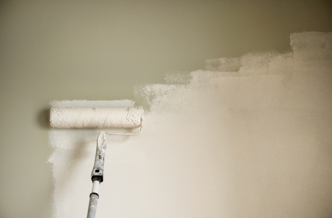 a roller with white paint painting a drywall